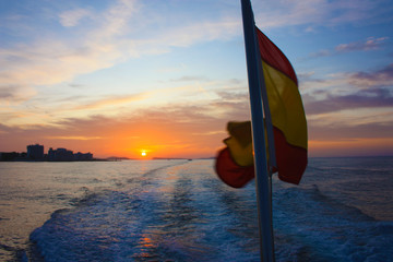 Wall Mural - red sunset on the horizon in zen on blue water in the southern sea of ​​spain with the Spanish flag flying in the wind