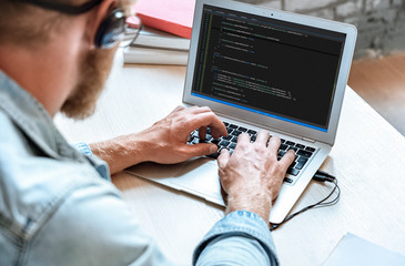 Over shoulder closeup view man IT coder programmer software engineer use laptop computer typing code develop program programming java language application on screen, web system app development concept