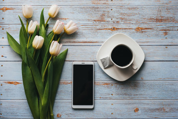 Wall Mural - White bouquet of tulips on blue wooden background with Cup of coffee and a smartphone