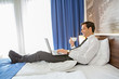© rilueda - Happy businessman in suit working on the hotel bed on his computer laptop notebook