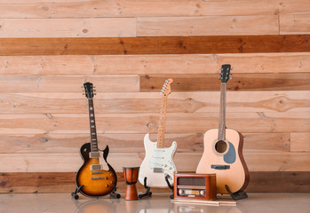 Modern guitars, drum and radio receiver near wooden wall