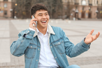 Poster - Young Asian man talking by mobile phone outdoors