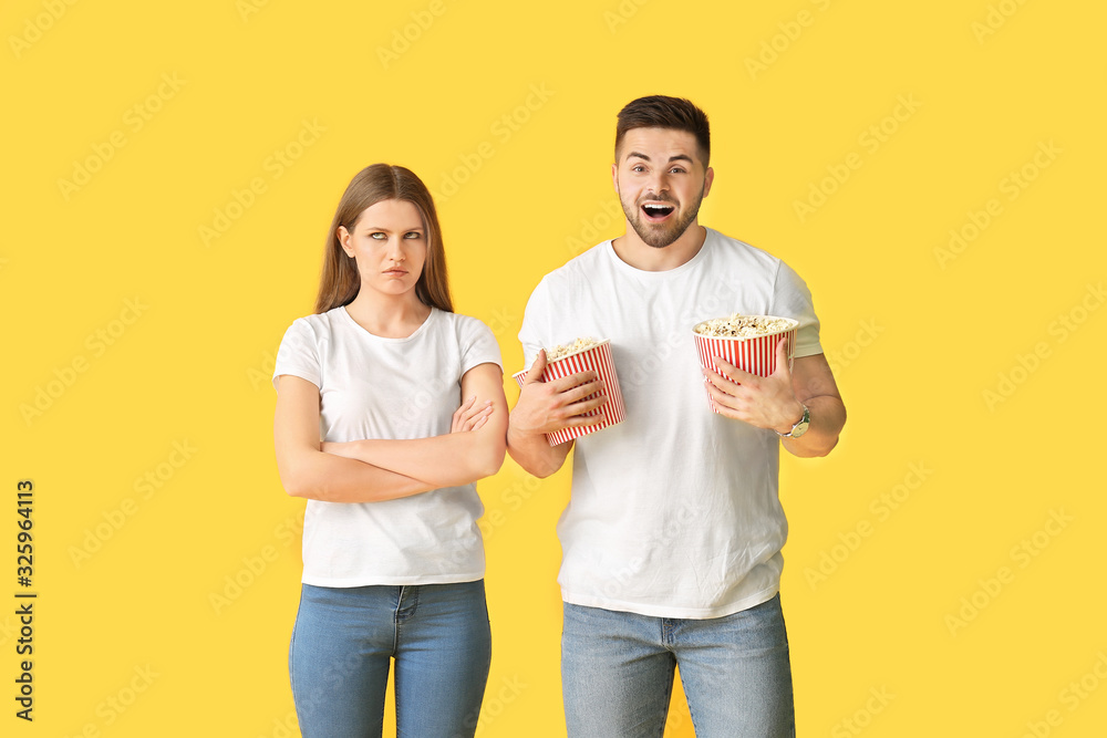Emotional young couple with popcorn on color background