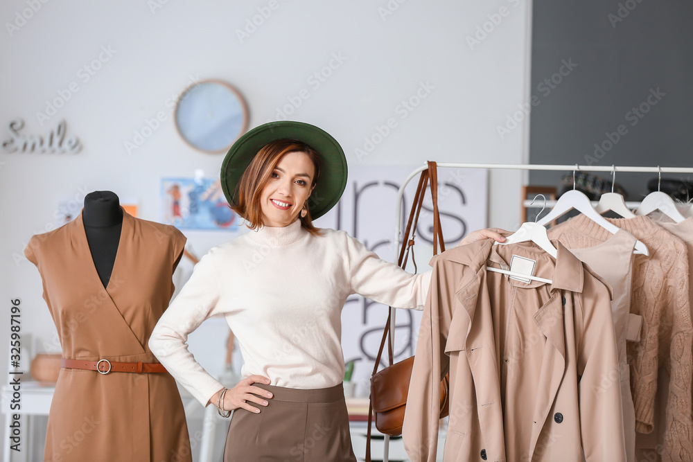 Female stylist near rack with modern clothes in her studio