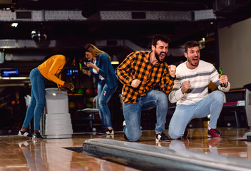 Wall Mural - Group of friends enjoying time together laughing and cheering while bowling at club.