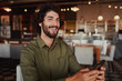 © StratfordProductions - Portrait of handsome young man laughing while reading funny message on phone sitting in modern cafeteria during free time