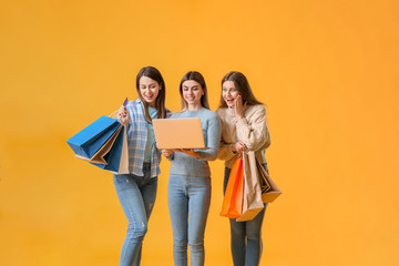 Sticker - Young women with laptop and shopping bags on color background