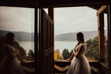 The Bride Is Standing Waiting For Her Groom On The Balcony Of His House. The Morning Of The Bride. She In A Pale Rose Wedding Dress Stands On A Beautiful Balcony Overlooking Lake And Mountains. 