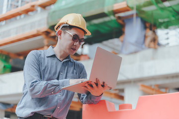 Young asian engineers are working on the construction site. Wear a yellow helmet safety. Hand holding computer laptop