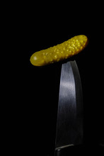  Pickled Cucumber On Sharp Knife Tip On Black Background. Dark Photo. Low Key Lighting. Copy Space. Minimalism.