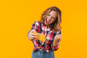 Wall Mural - Image of young woman wearing plaid shirt rejoicing and holding cellphone