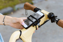 Woman Hand Uses The Phone. The Smartphone Is Attached To The Bicycle Steering Wheel