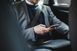 © Maskot - Midsection of mature businessman using phone while sitting in car