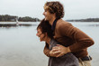 © Maskot - Smiling woman giving piggyback ride to male friend by sea against sky
