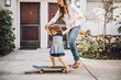 © Maskot - Smiling daughter balancing over skateboard with help of mother on footpath