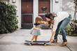 © Maskot - Daughter skateboarding with help of smiling mother on footpath