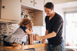 © Maskot - Happy father looking at daughter pushing french press while sitting on kitchen counter