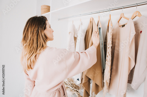 Cuadros en Lienzo Cute young woman standing in front of hanger rack and trying to choose outfit