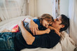 © Maskot - Mature father with eyes closed kissing daughter while lying on bed