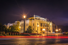 The Building Of Rudolfiunum Concert Halls On Jan Palach Square In Prague, Czech Republic - Night View. Czech Philharmonic Orchestra With Light Trails From Passing Cars.