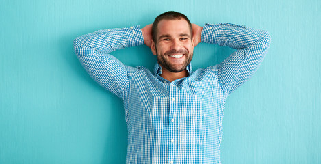 Wall Mural - Happy man with hands behind head in front of blue wall