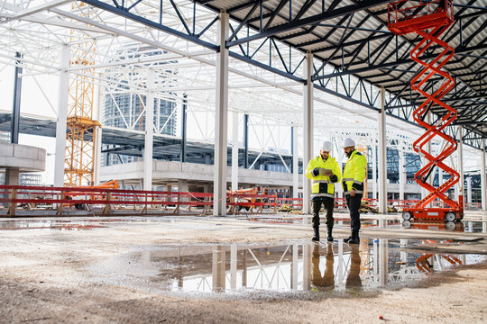 Men engineers standing outdoors on construction site, using tablet.