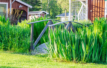 Decorative old wooden bridge with rails standing in the middle of high green grass at trimmed lawn, Vasterbotten, Northern Sweden, Umea