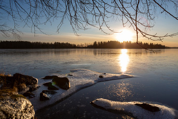 Wall Mural - Wintry landscape from Finland during February. Cold afternoon sunset scenery. Frozen lake shore.