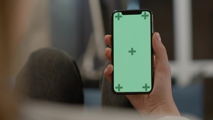 close up view of woman at modern room lying on a sofa using phone with green mock-up screen chroma k