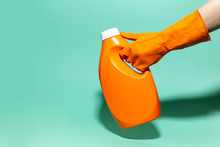 Close-up Of Female Hand Wearing Orange Cleaning Glove, Holding Detergent Bottle On Background Aqua Menthe Color.