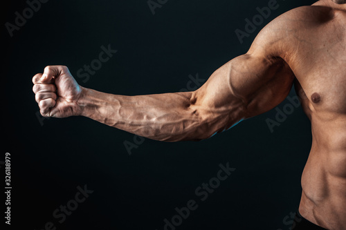 Fotografía tense arm clenched into fist, veins, bodybuilder muscles on a dark background, isolate