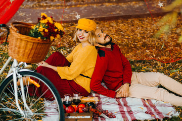 Young family couple have picnic in autumnal park. Man and woman sitting on picnic blanket. Bicycle ride and active lifestyle.