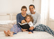 © SB Arts Media - Dad, mum and young daughter reading a book together. Lifestyle image of happy Family having fun reading fairy tales in bed at home. In happy family, parenting and education concept.
