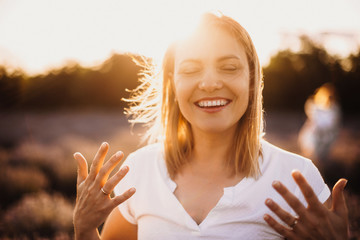 charming caucasian mother smiling and gesturing against the sunshine with a lavender field on backgr