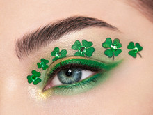 Conceptual Photo Of St. Patrick's Day. The Eye Of The Young Beautiful Woman With Bright Green Shadows And Expressive Eyebrows. Shamrock Patterns. Holiday Makeup