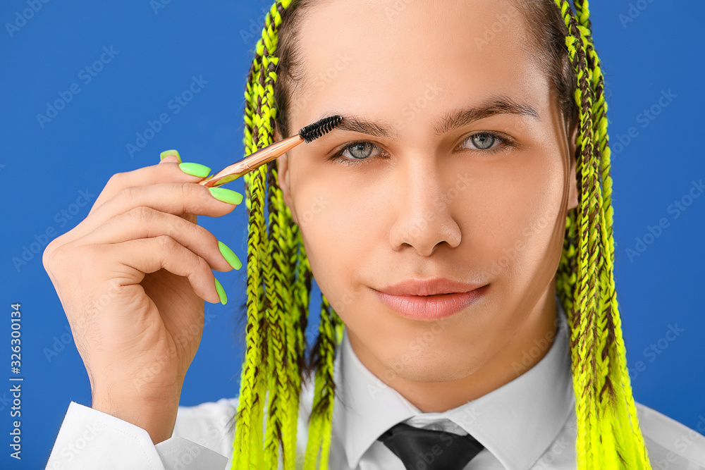 Transgender woman applying makeup against color background