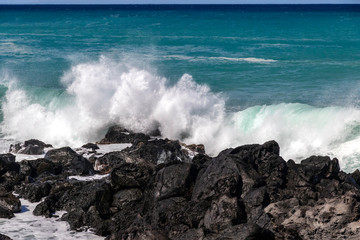 Wall Mural - White wave breaking against black volcanic rocks  on the Kona coast of Hawaii's Big Island. Vivid blue-green pacific ocean in the distance.