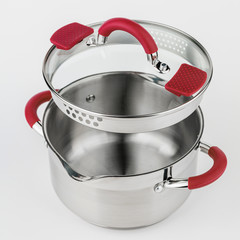 Stainless casserole with glass lid and red handles on grey background.