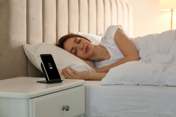 Smartphone charging on wireless pad and woman sleeping in bed