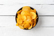Tasty potato chips in bowl on white wooden background. Top view