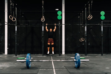 Wall Mural - Young muscular man training on bar in a gym