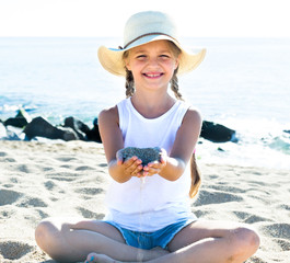 baby girl in hat playing with sand on sea coast in summer