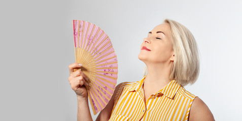 Attractive middle aged woman relaxing with fan. Mature woman experiencing hot flush from menopause isolated