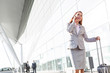 © MDBPIXS - Young attractive businesswoman talking on smartphone while walking with her suitcase in airport