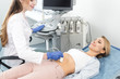 © LIGHTFIELD STUDIOS - smiling beautiful doctor examining stomach of female patient with ultrasound scan in clinic