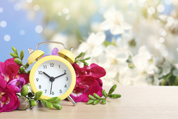 Poster - Alarm clock and flowers on wooden table against blurred background, space for text. Spring time