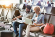 © moodboard - Mature woman working on her laptop,  husband is reading newspaper while waiting for boarding in airport