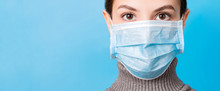 Portrait Of Young Woman Wearing Medical Mask At Blue Background. Protect Your Health. Coronavirus Concept
