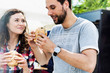 Young attractive couple eating hamburgers against food truck with lens flare in background