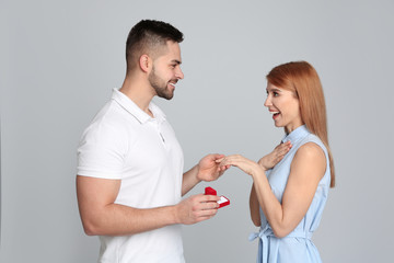 Wall Mural - Man with engagement ring making marriage proposal to girlfriend on light grey background